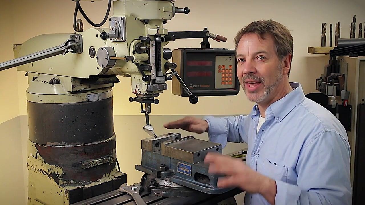 The presenter, standing beside a milling machine with a vise and digital readout, encourages viewers to apply the tips in their own workshops. The environment is a well-equipped machine shop, and the presenter is gesturing enthusiastically, reinforcing the message to build something cool.