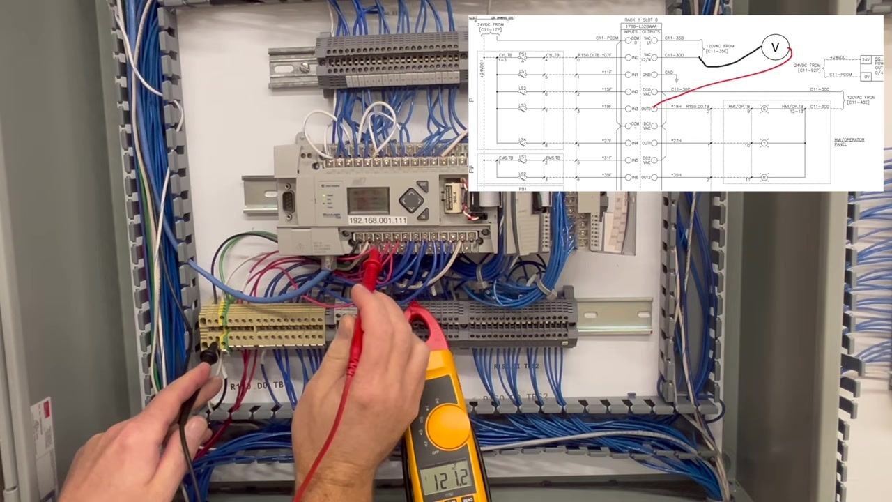 Control panel with the PLC and wiring visible, meter resting on the terminal block and displaying 0.0V, no probes held.