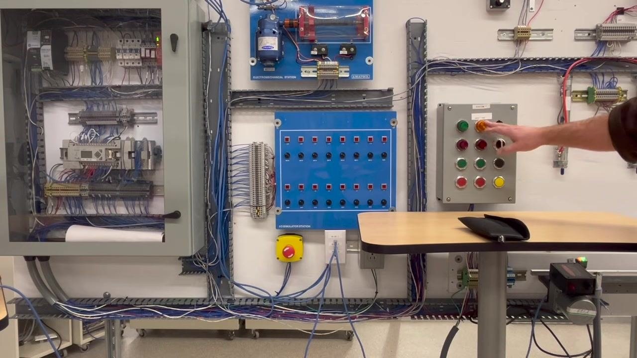 A hand holding a Fluke 365 True RMS Clamp Meter set to measure AC voltage, with the back of the control panel exposed to show wiring and relays.