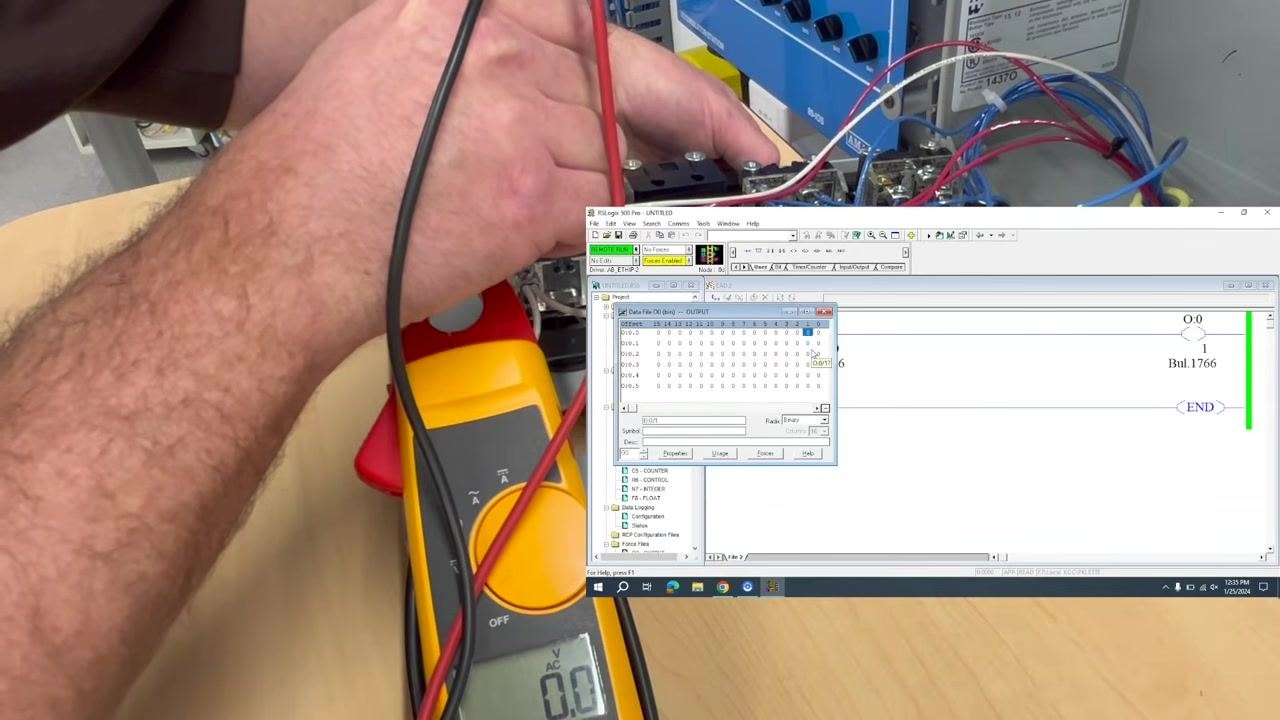 The clamp meter is positioned near the output terminals, still reading 0.0V AC. A schematic diagram overlay shows where to measure voltage.