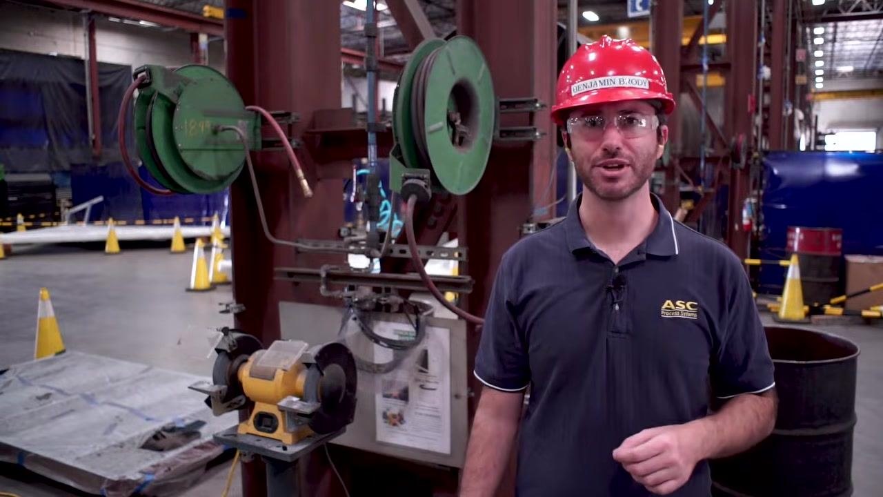 A worker demonstrates safe operation near a bench grinder, using tools and cooling water as part of the grinding process.