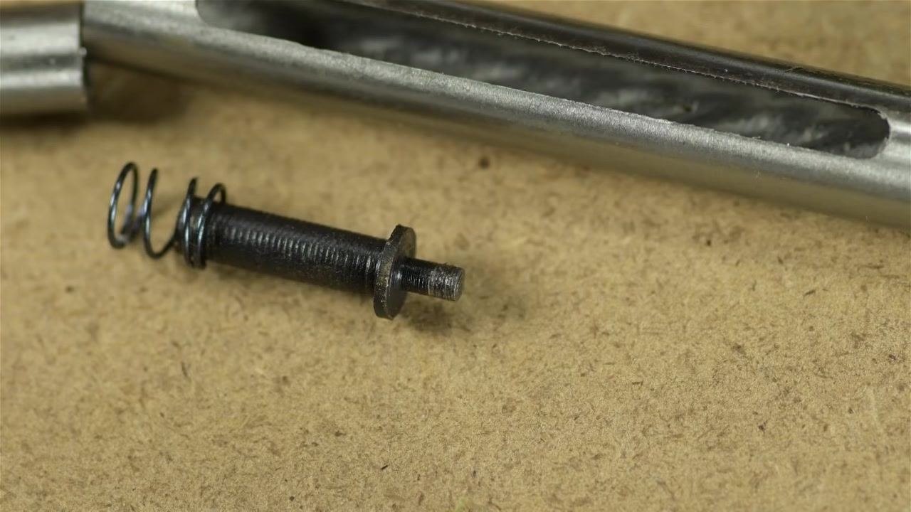 Close-up of the retainer pin with spring and the slotted plunger body resting on a tan work surface, showing machining marks and the visible slot.