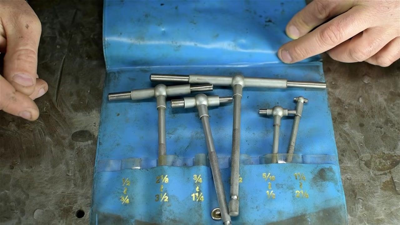 A blue vinyl pouch containing a set of telescoping bore gauges of various sizes, with size labels visible and a hand on each side of the pouch.