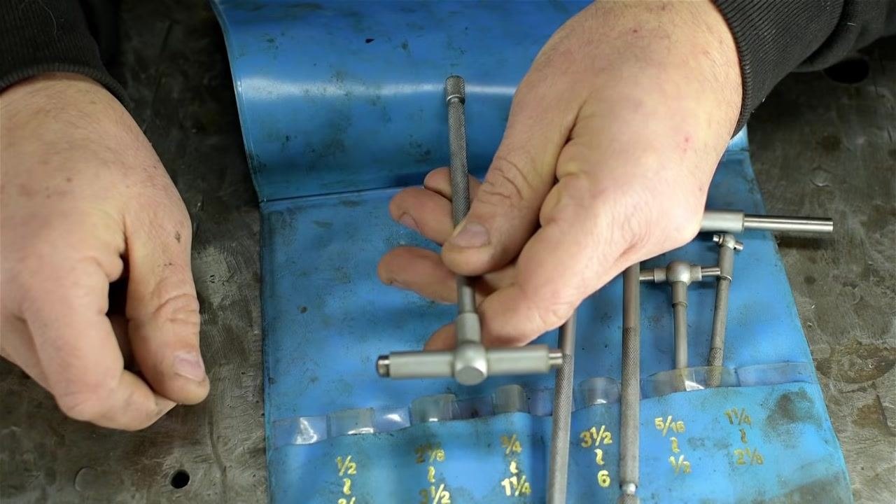 Hands holding a telescoping bore gauge horizontally above the blue pouch, illustrating the tool's use for transferring internal dimensions.