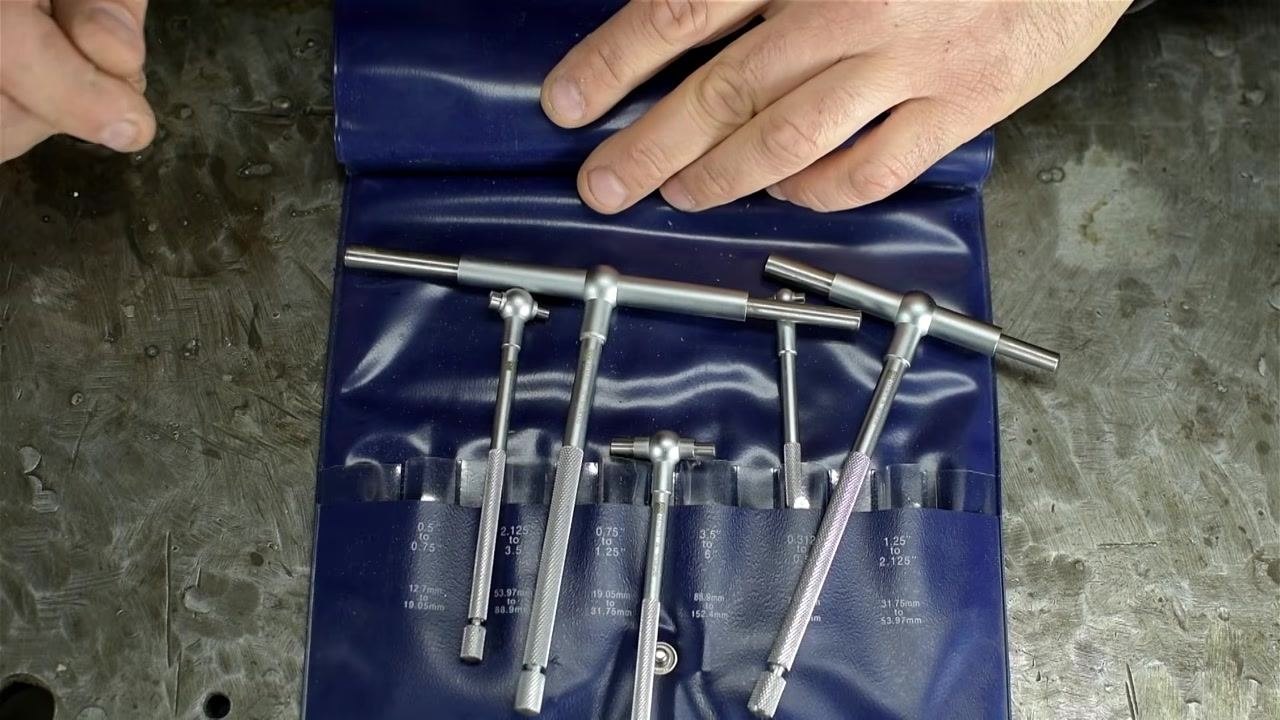 Hands holding a telescoping bore gauge above a blue pouch, pointing at the locking mechanism to check proper locking force, with several gauges visible in the background.