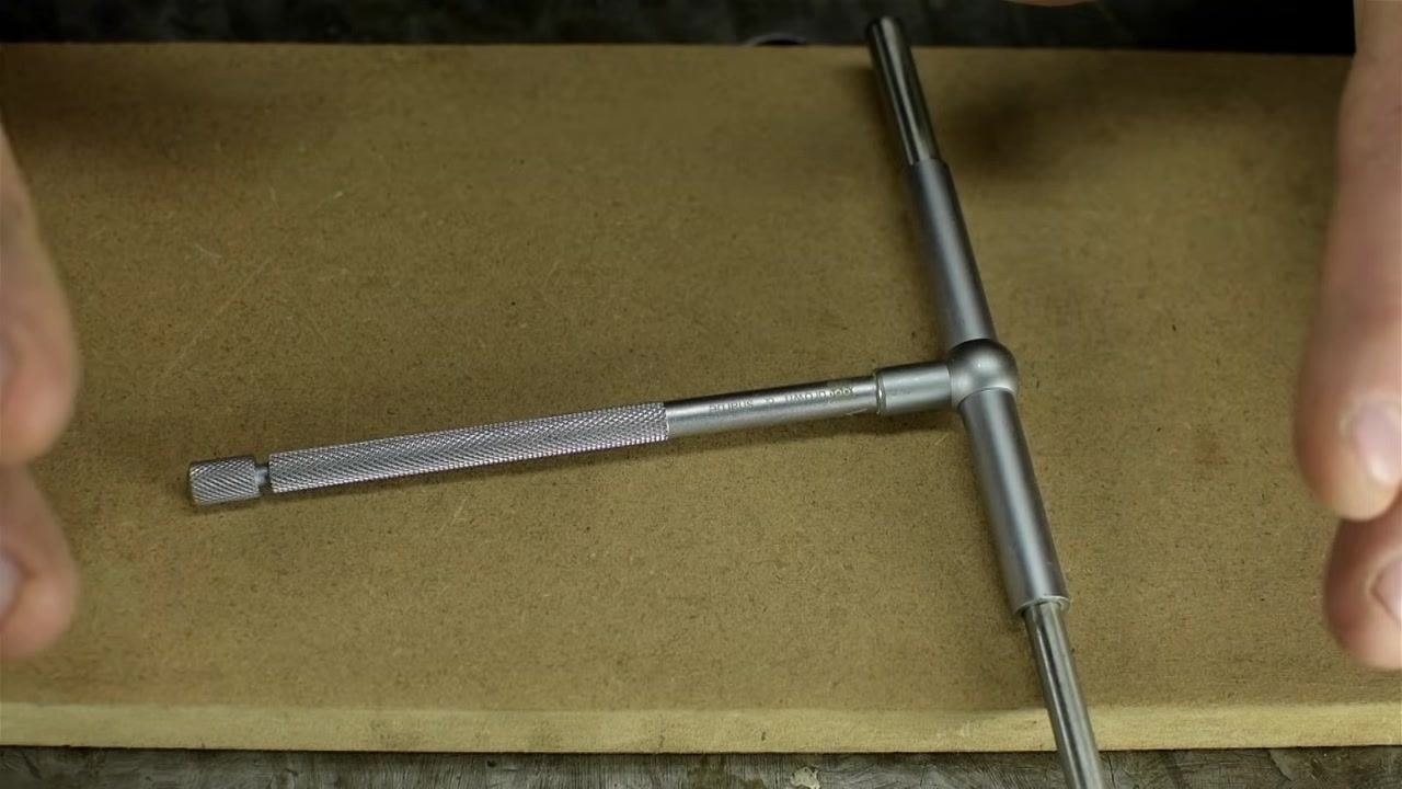 A telescoping bore gauge lying on a tan work surface, with the knurled locking knob visible at the end of the handle.