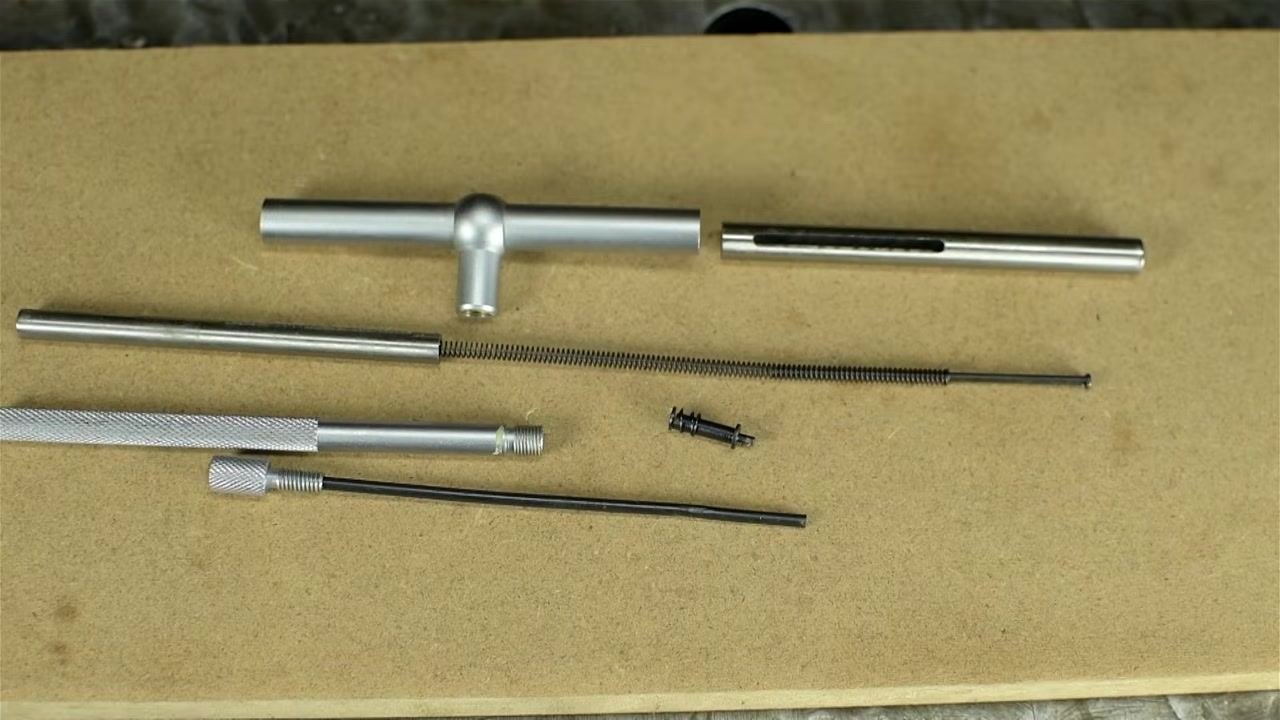 A telescoping bore gauge clamped in a vise with orange soft jaws, ready for safe disassembly, with a hand steadying the tool.