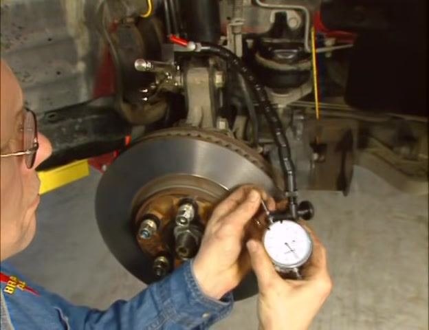 Person positioning the dial indicator and flex arm near the brake rotor, ensuring the setup can reach the rotor's friction surface.