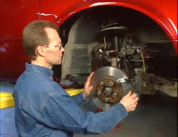 Technician rotating the brake rotor by hand while observing the dial indicator to find the high spot.