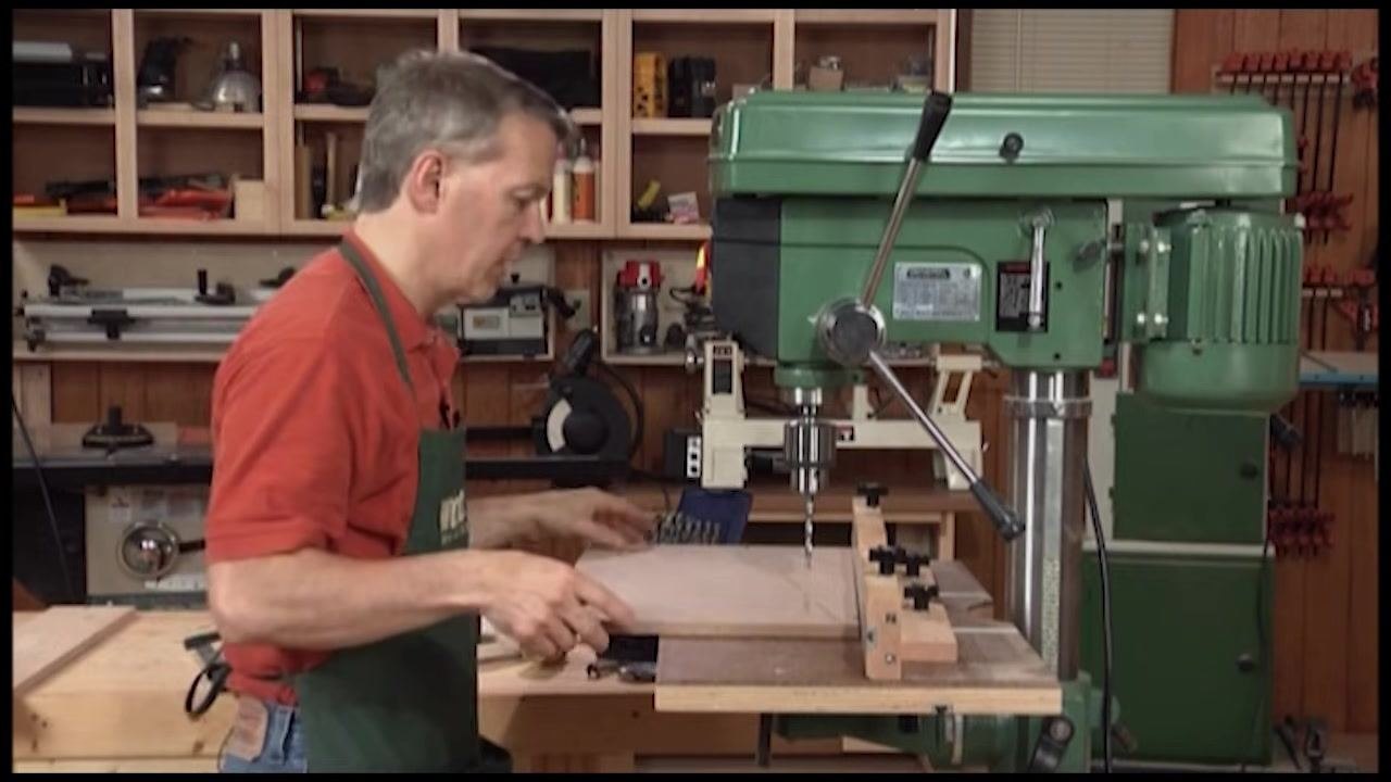 Close-up of a drill bit creating a hole in a piece of wood, with wood shavings accumulating around the hole