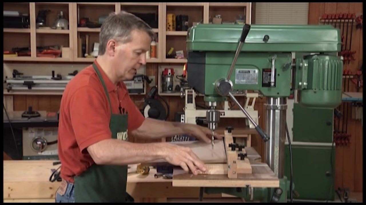 Operator drilling through a workpiece with scrap wood underneath to protect the table
