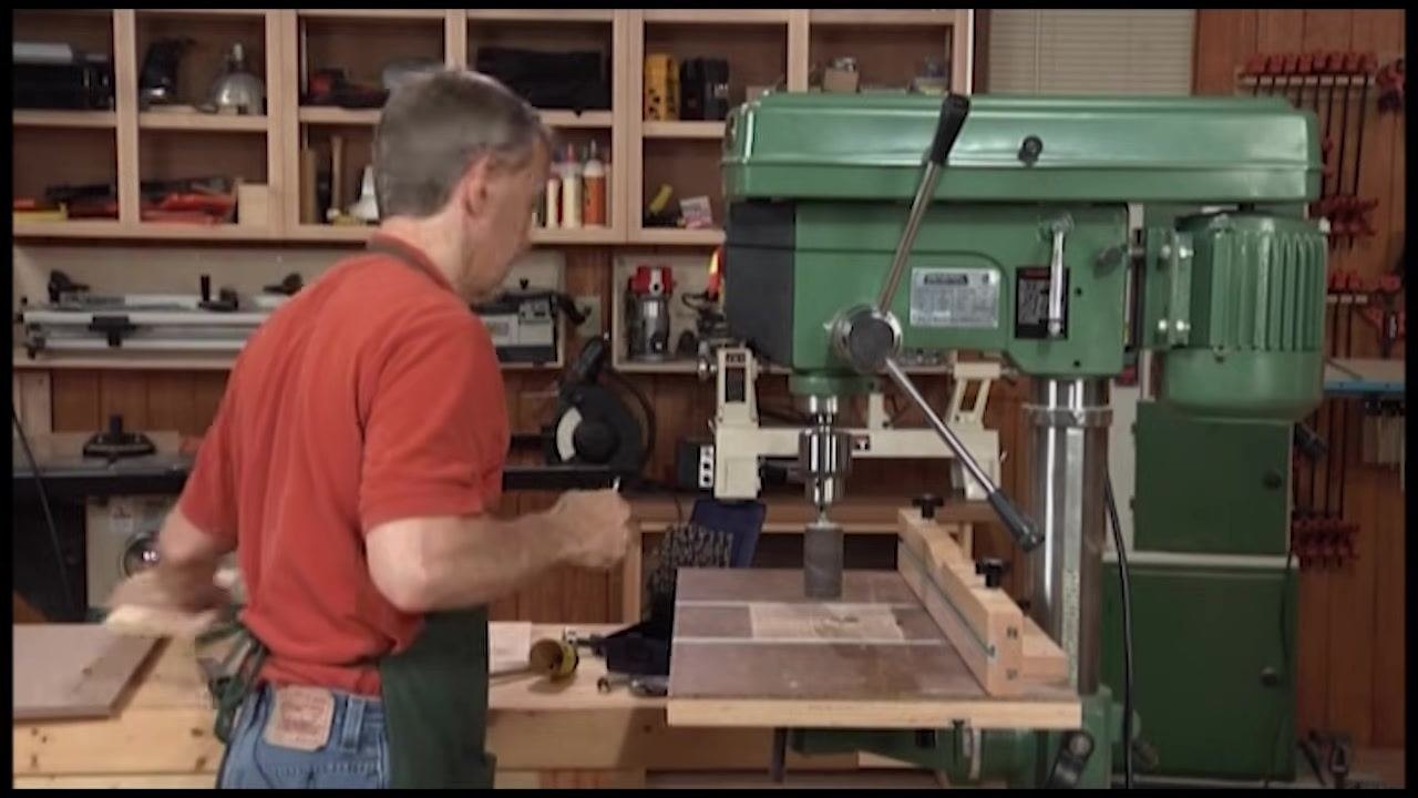 Operator aligning a wooden workpiece with a curved cutout against the drum sander, with the pencil line visible