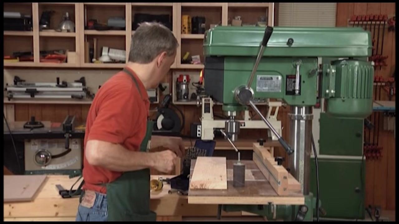 Operator preparing a rectangular wooden workpiece with a curved cutout for sanding with the drum sander