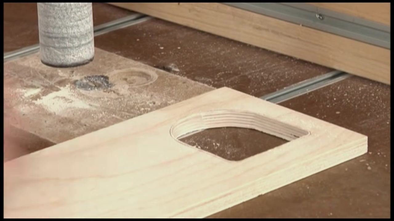Hands positioning a wooden workpiece with a curved cutout near the drum sander, preparing to add a stop block