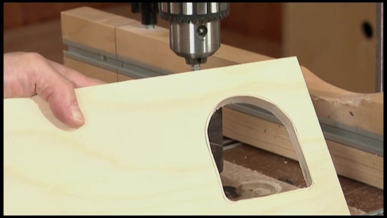 Close-up of a hand holding a wooden workpiece with a curved cutout near the drum sander, with the pencil line visible
