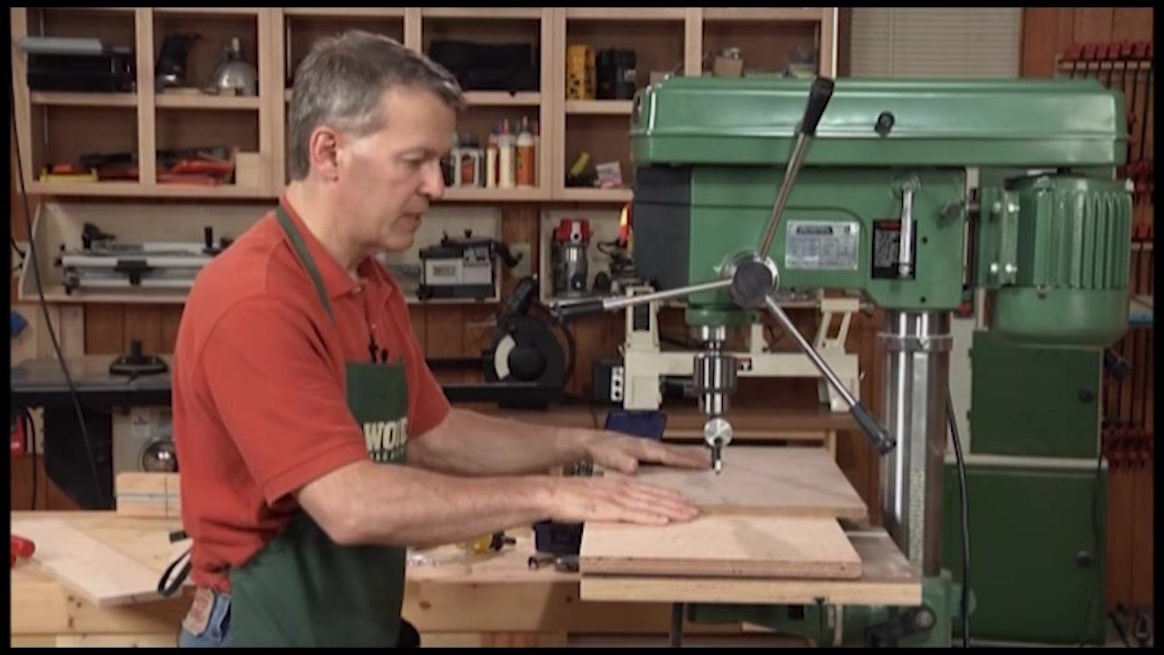 Large wooden board positioned on the drill press table, extending beyond the fence
