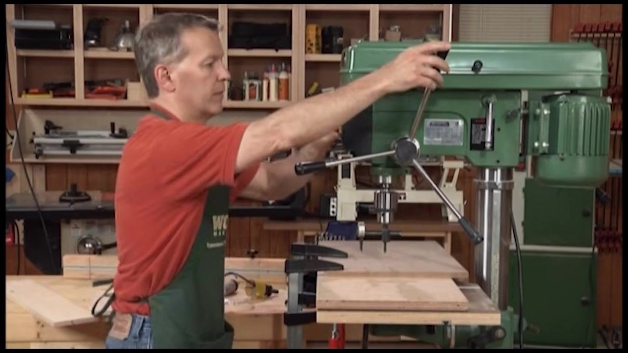 Operator adjusting and locking the fence on the drill press table with the workpiece clamped in place