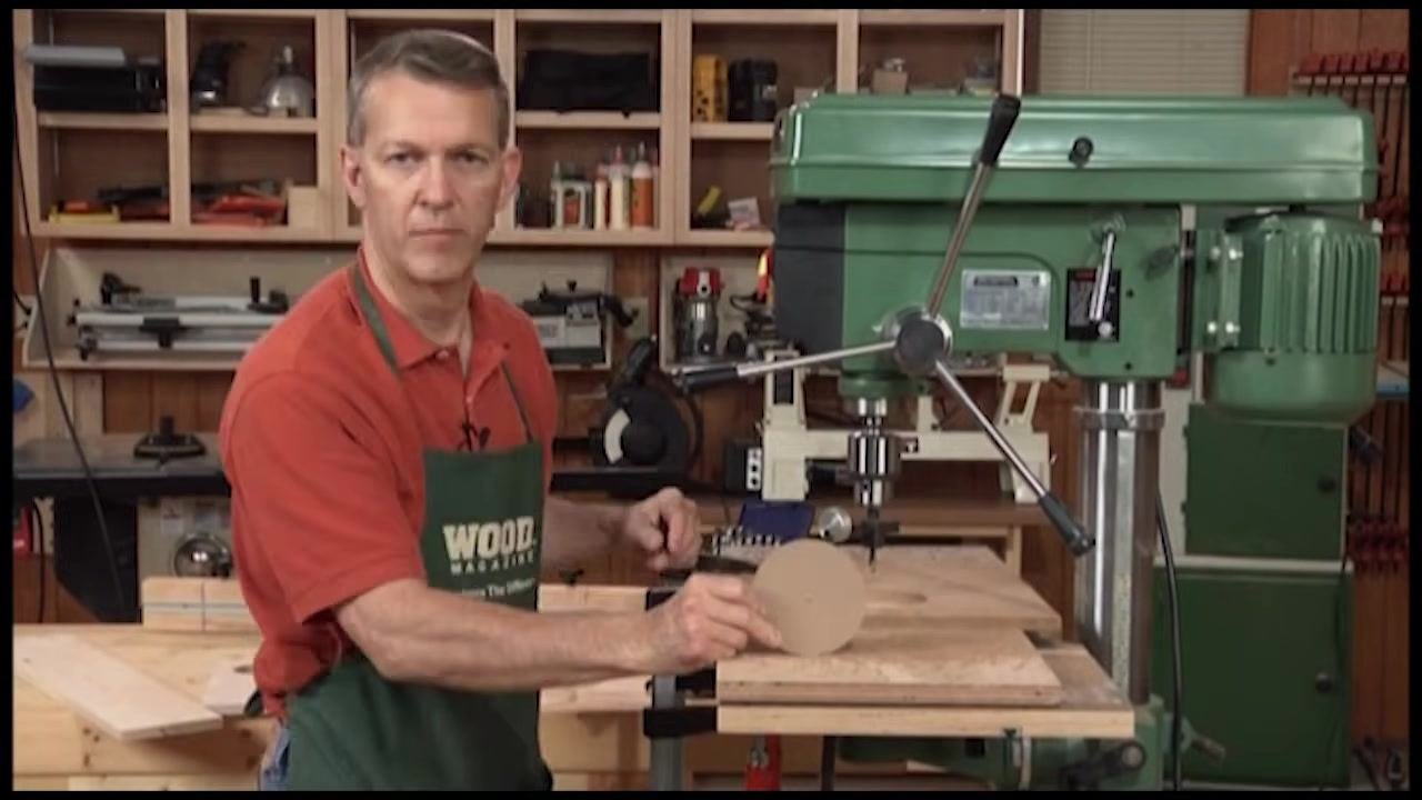 Hand lifting a perfectly cut wooden circle from the opening, with the circle cutter still attached to the drill press