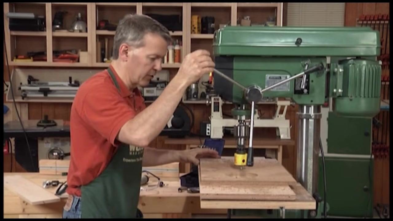 Wooden workpiece clamped to the drill press table with a yellow hole saw attached