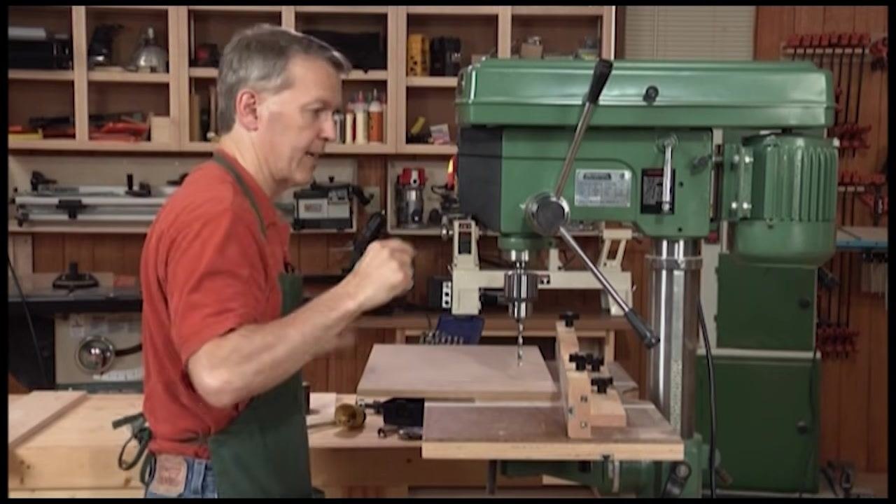 Operator positioning the workpiece under the drill bit with the handle removed, aligned with the fence and stop blocks