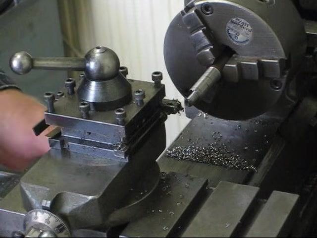 Operator's hand near the retracted tool post while the lathe is still running.