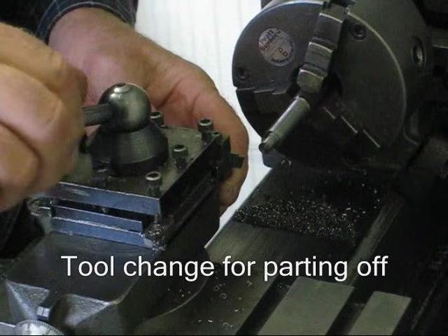 Lathe engine running with the spindle spinning, tool post and workpiece visible, and metal chips present.