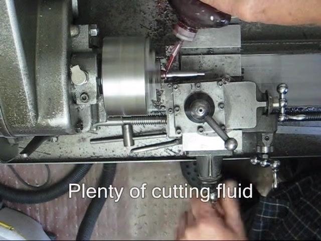 Operator using a caliper to measure the workpiece held in the chuck, with the tool post visible in the foreground.