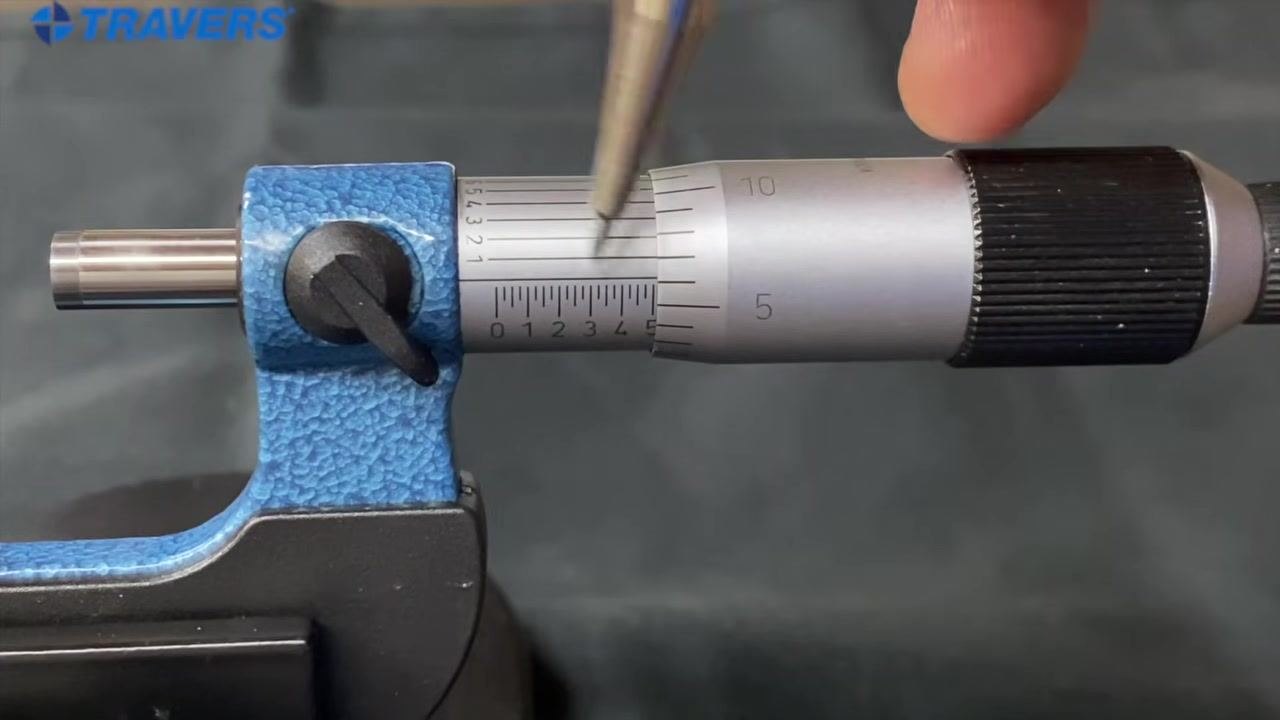 Micrometer close-up: the sleeve shows the "5" mark, the thimble shows "5" aligned with the reference line, and a pen points at the auxiliary scale.