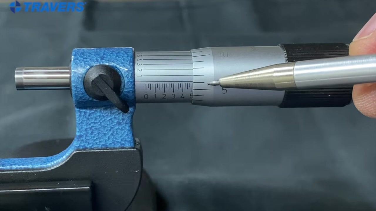 Micrometer close-up with a pen pointing at the thimble scale just past the 5 mark, with the sleeve scale visible.