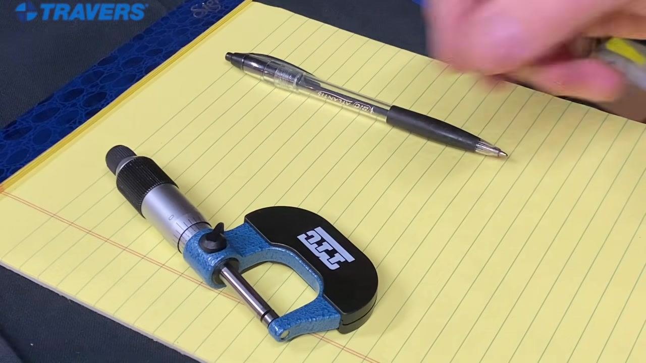 A hand reaching for the micrometer on a yellow legal pad, with a pen nearby.