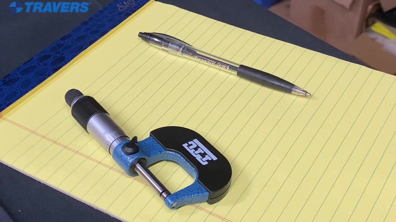 Instructor clarifying terminology, workbench with micrometers, American flag and toolbox in background