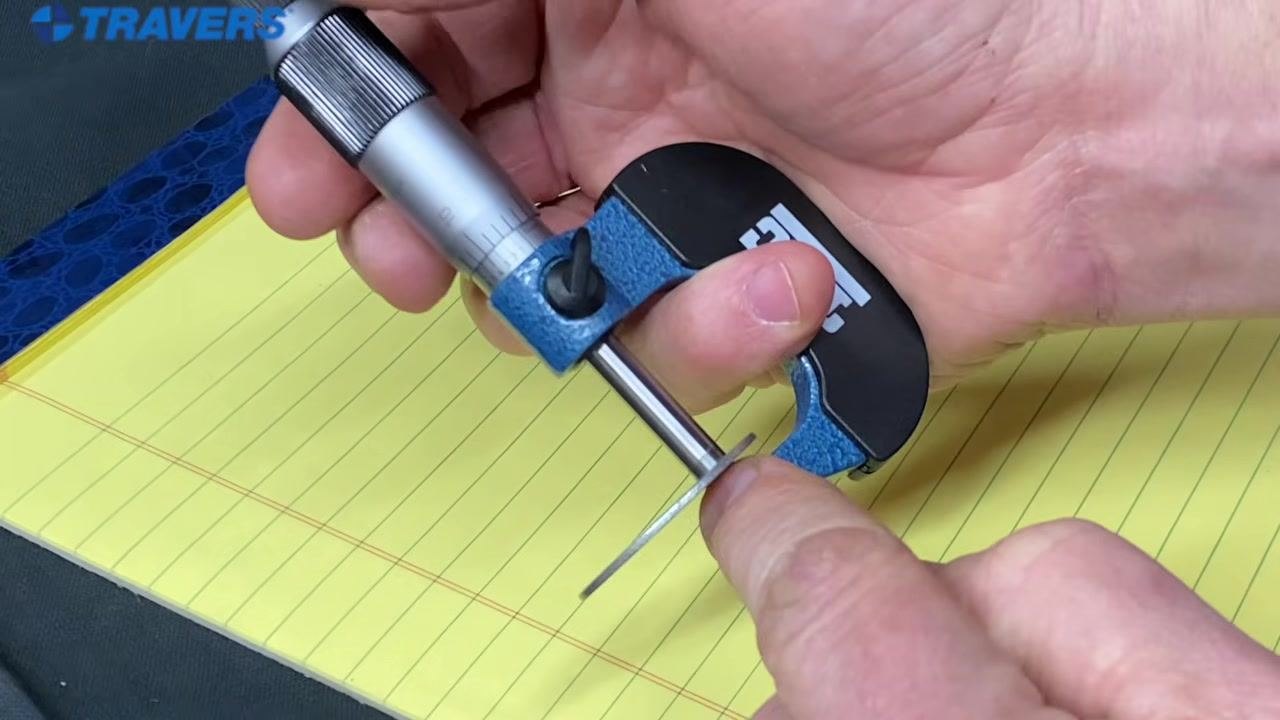 A hand securely holding the micrometer, with the ring finger on the thimble, ready for measurement.