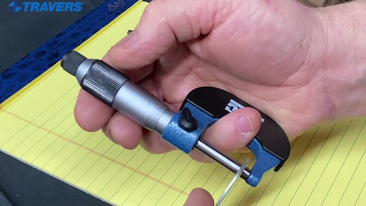 A hand holding the micrometer with the frame in the palm and the ring finger resting on the thimble.