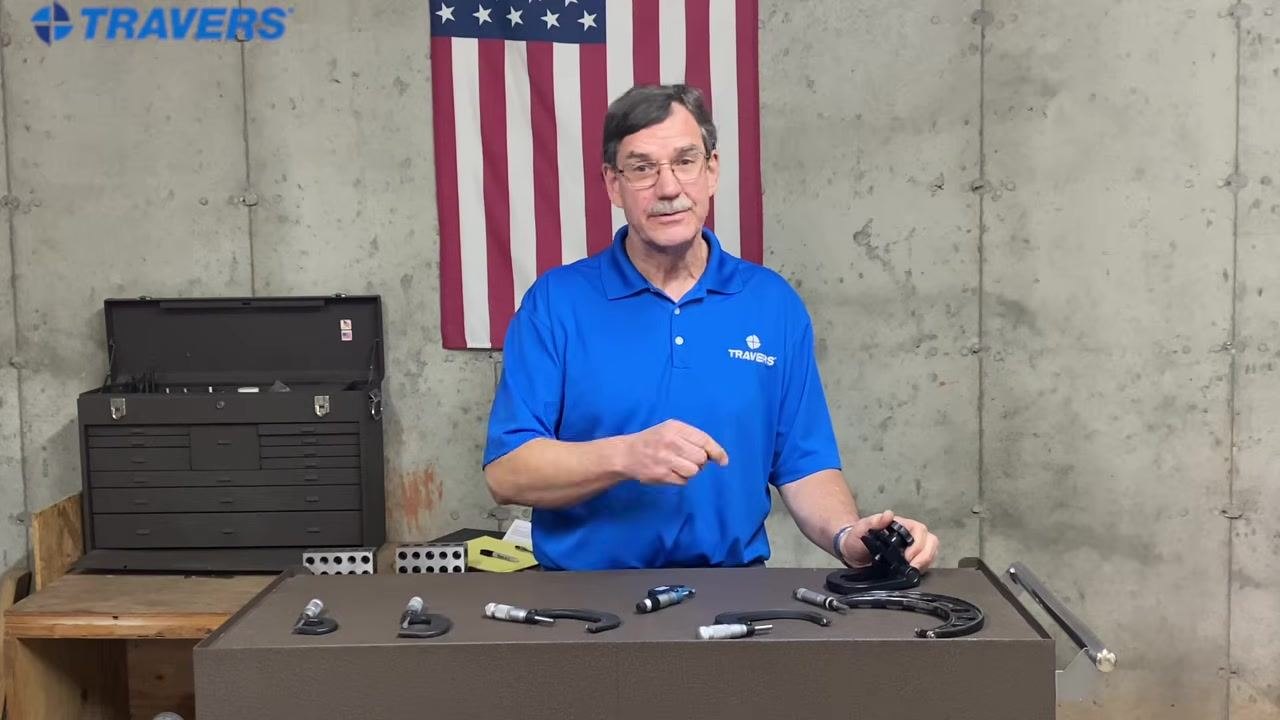 Instructor explaining with hand gestures, workbench with micrometers, American flag and toolbox in background