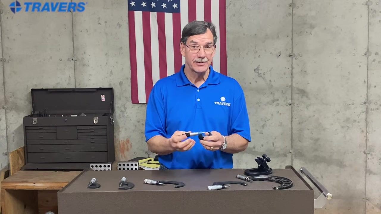 A hand holds a micrometer to show its overall size and parts, with several micrometers and tools laid out on the table.
