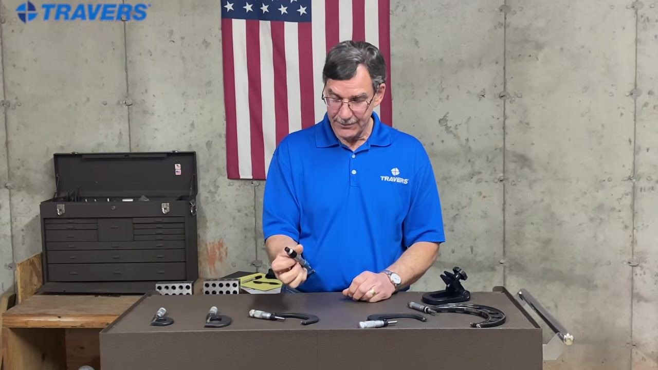 The instructor stands behind the workbench, holding a micrometer and addressing the viewer, suggesting further resources.