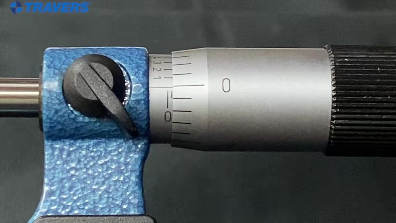 Micrometer close-up showing the "1" mark just appearing on the sleeve, indicating 0.100 inches, while a hand turns the thimble.