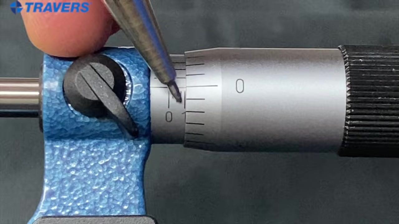 Close-up of a micrometer with a pointer indicating the "1" mark just emerging on the sleeve and the "0" on the thimble aligned with the reference line.