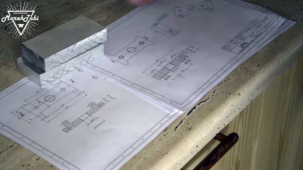 Technical drawings and billets laid out on a work surface, showing detailed dimensions and section views with three metal billets stacked on the left.