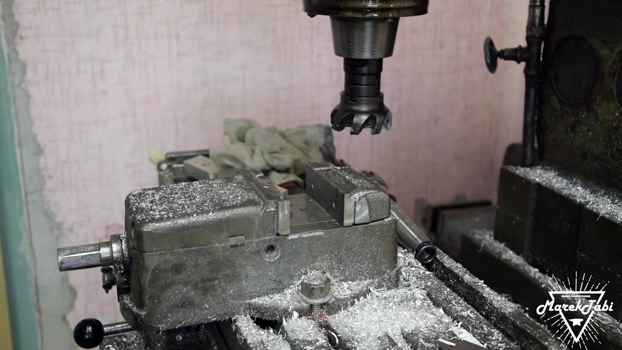 An operator positioning a machined billet in the vise, ensuring it is properly aligned and clamped, with drilled holes and a clean machined surface visible.
