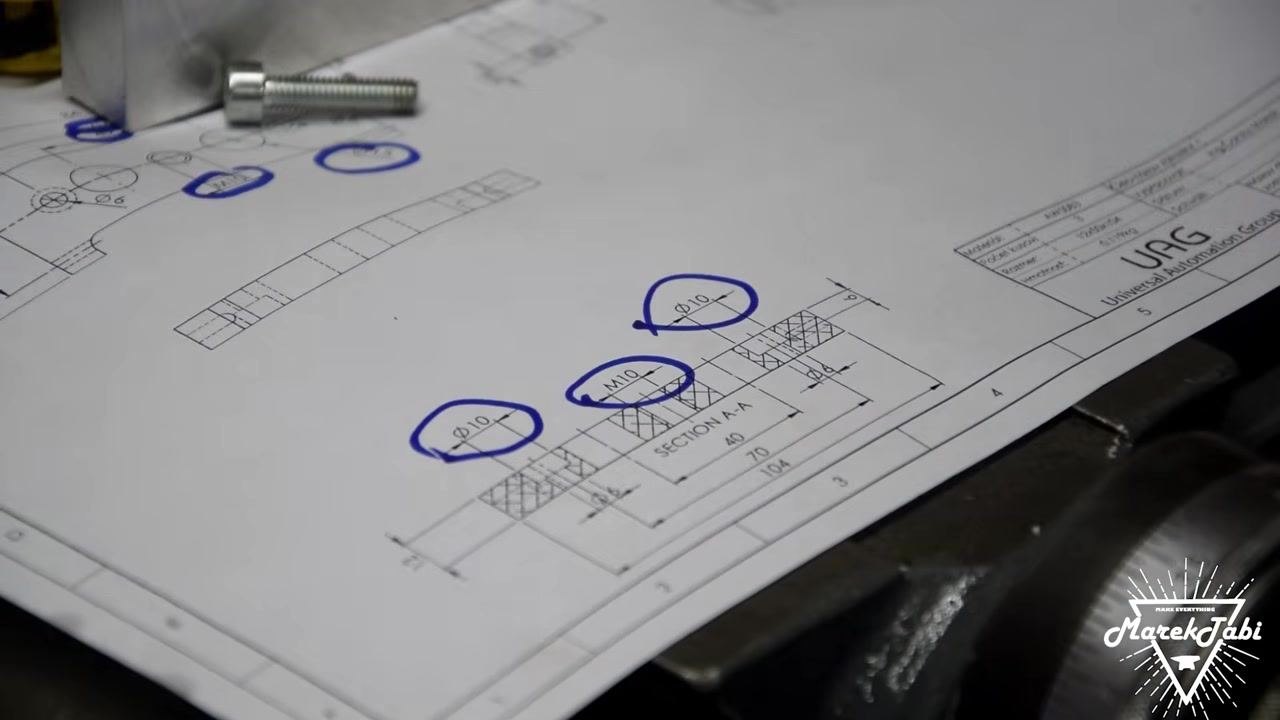 A technical drawing with key dimensions and hole locations circled in blue marker, with the billet and a bolt placed on the drawing for reference.