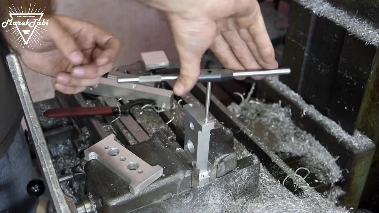 A tap wrench being positioned into the drilled hole of the workpiece, preparing to cut threads, with the operator's hands guiding the tool.