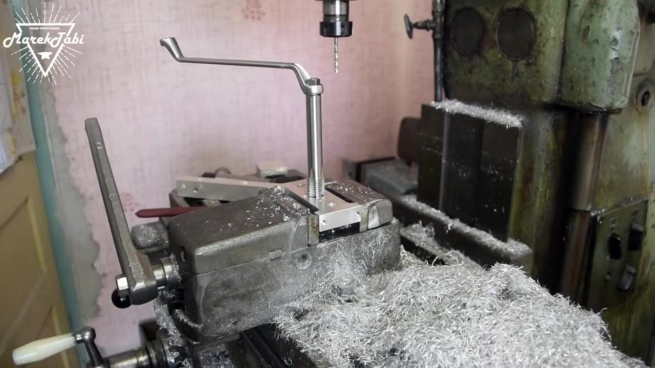 A close-up of the tap wrench being turned by hand, cutting threads into the hole of the metal workpiece clamped in the vise.