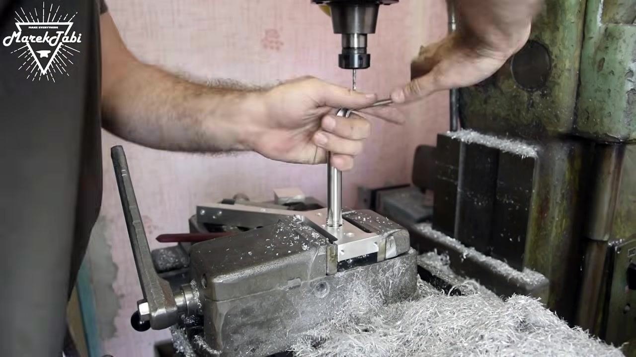 A wide view of the work area showing the tap wrench fully engaged in the workpiece, with metal shavings scattered around.