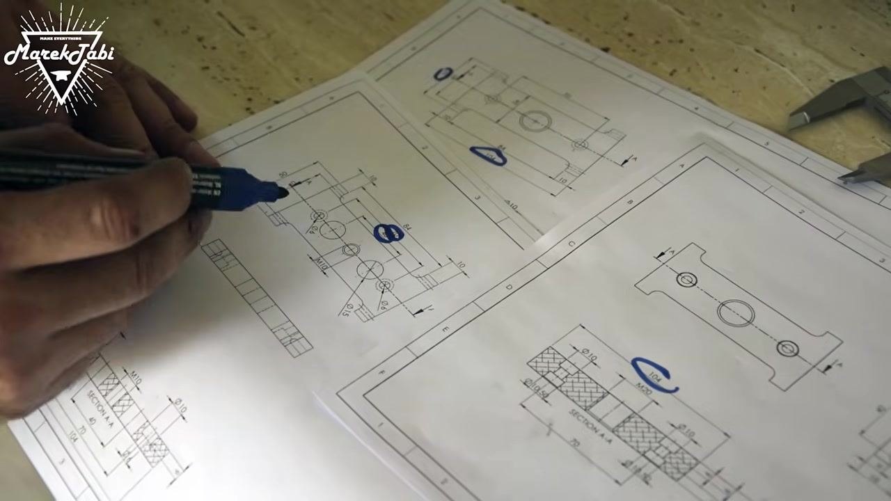 An operator continuing to mark technical drawings, highlighting additional features and dimensions, with calipers visible on the work surface.