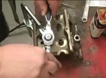 A ratcheting tap handle being used to turn a tap into a metal workpiece, with tools and oil visible on the workbench