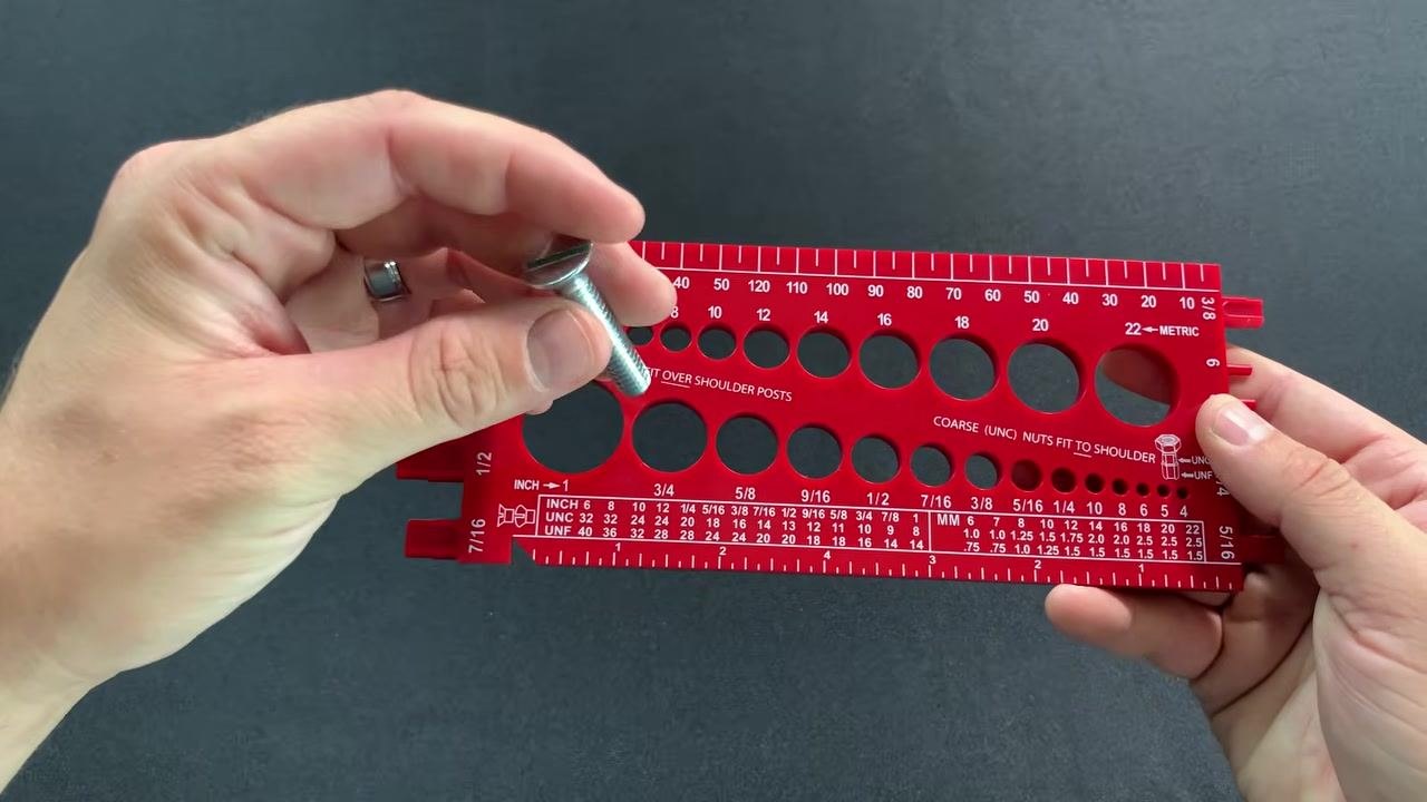 A slotted flathead machine screw held above the red gauge, with the head clearly visible, indicating the entire length will be measured.
