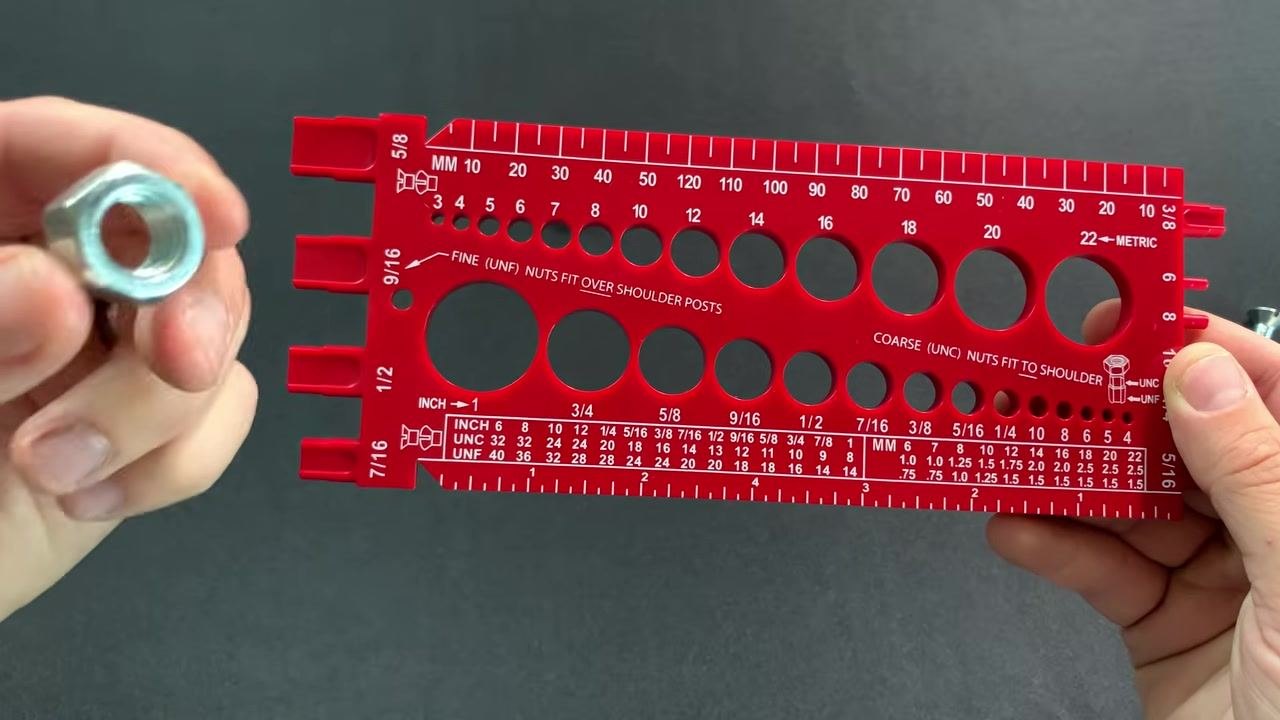 A nut held in the left hand next to the red bolt gauge, not inserted, indicating it did not fit all the way down in the coarse section.