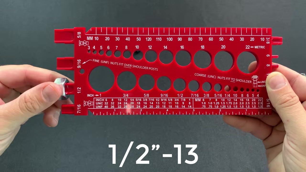 A nut inserted into the 1/2 inch coarse thread hole of the red bolt gauge, with "1/2”-13" text overlaid, held with both hands.