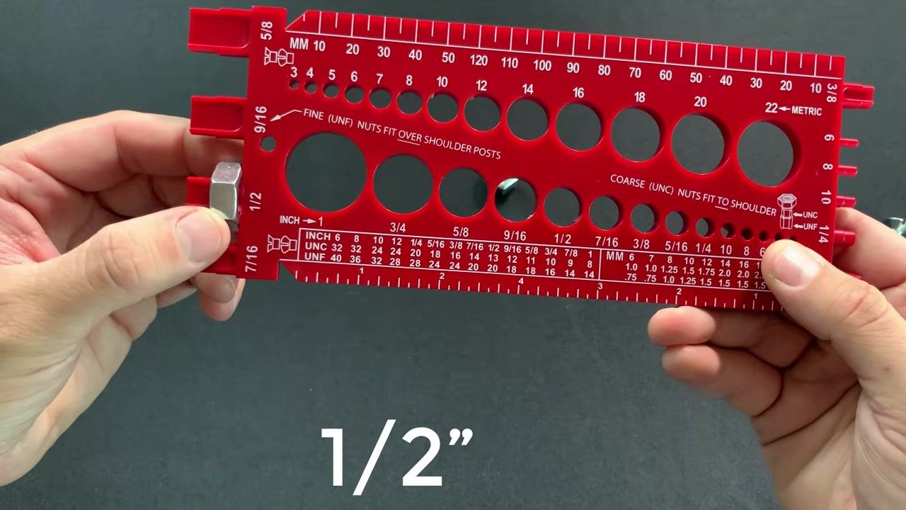 A nut fully inserted into the 1/2 inch fine thread hole of a red bolt gauge, held with both hands, with "1/2”" text overlaid.